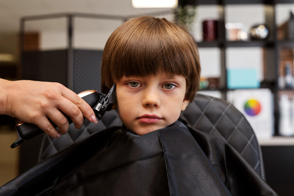 little boy sitting on barber chair having a Classic Bowl Cut 