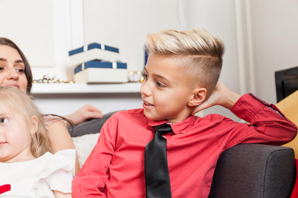 Toddler boy sitting on a couch with family having quiff hairstyle